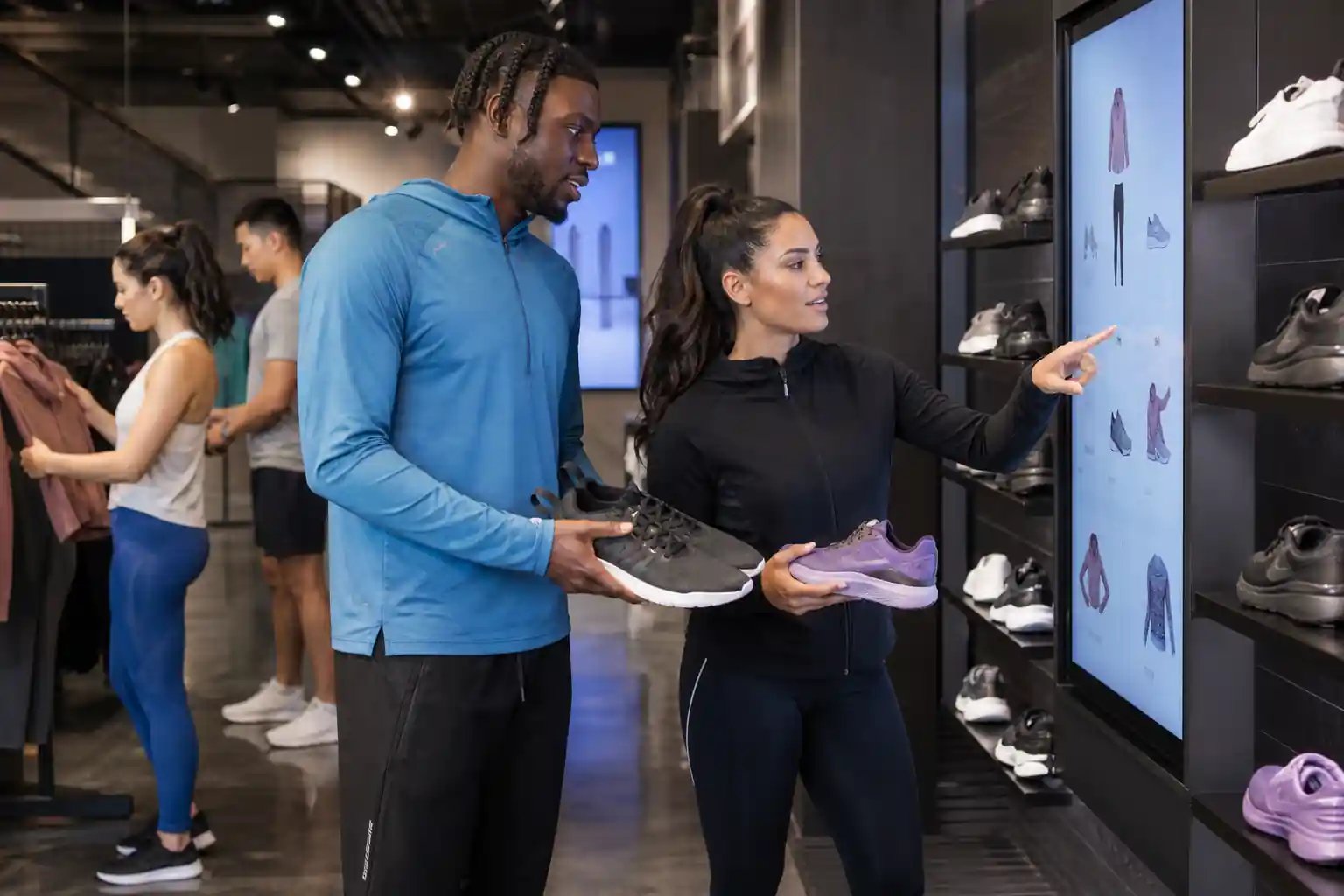 Athletic and performance wear shoppers interacting with personalized AI recommendations on digital screens in a sleek sports retail environment, with running shoes, leggings and jackets displayed under dynamic lighting.